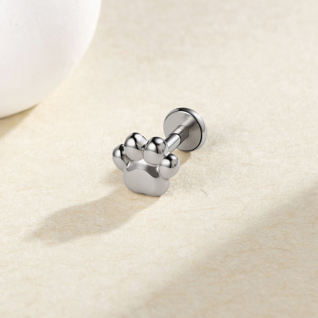 Silver-colored paw-print flat-back stud on a cream surface